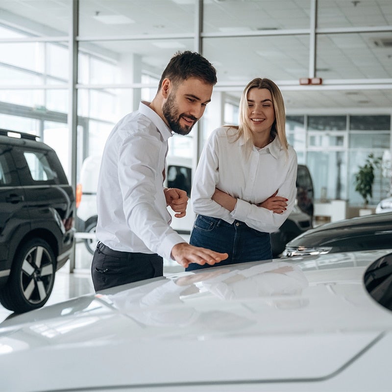 Salesman guiding a woman inside a car showroom