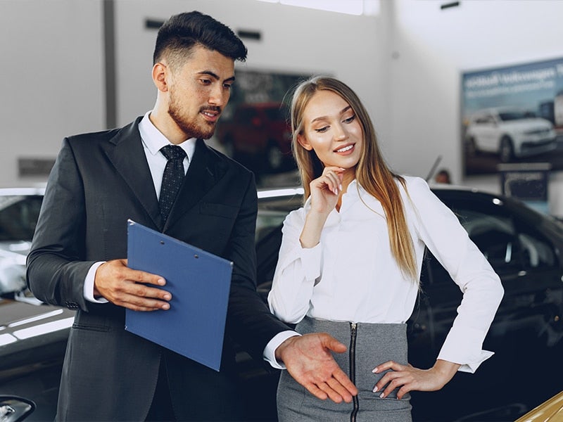 Salesman guiding a woman inside a car showroom