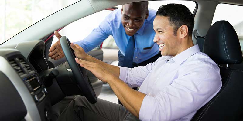 Smiling man in driver’s seat with cheerful salesman outside